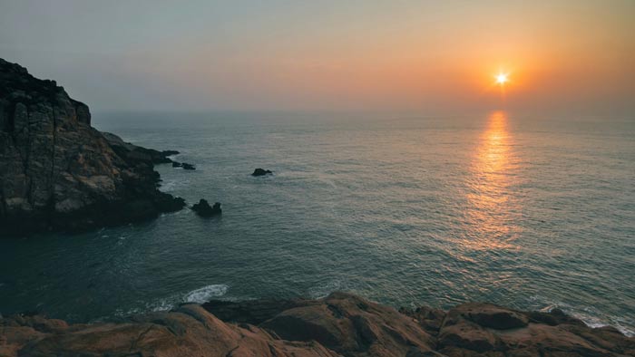 Sunset over a calm ocean with rocky coastline, reflecting soft golden light on the water surface. Beautiful seascape capturing nature's tranquility.