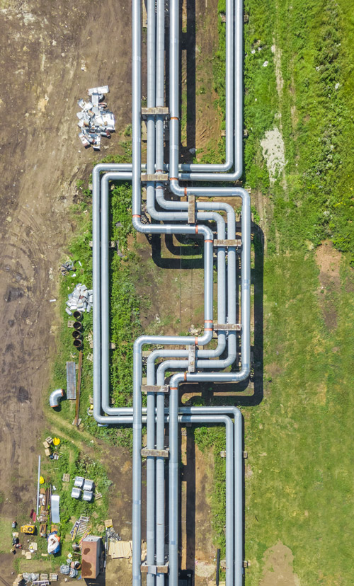 Aerial view of extensive industrial pipes running through a green landscape, with construction materials and equipment visible nearby.