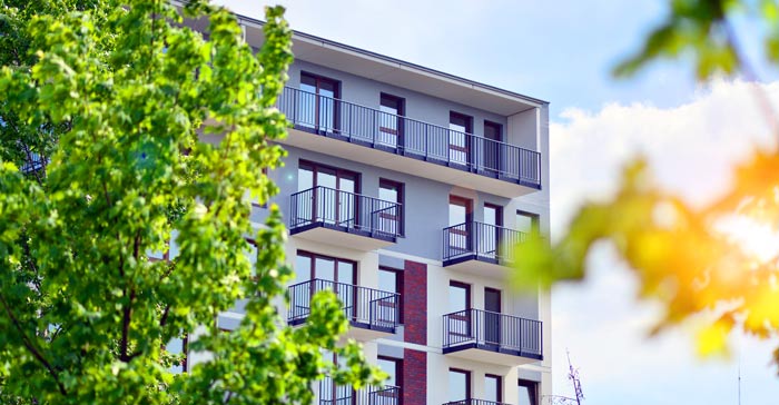 Modern apartment building surrounded by green trees and a blue sky.